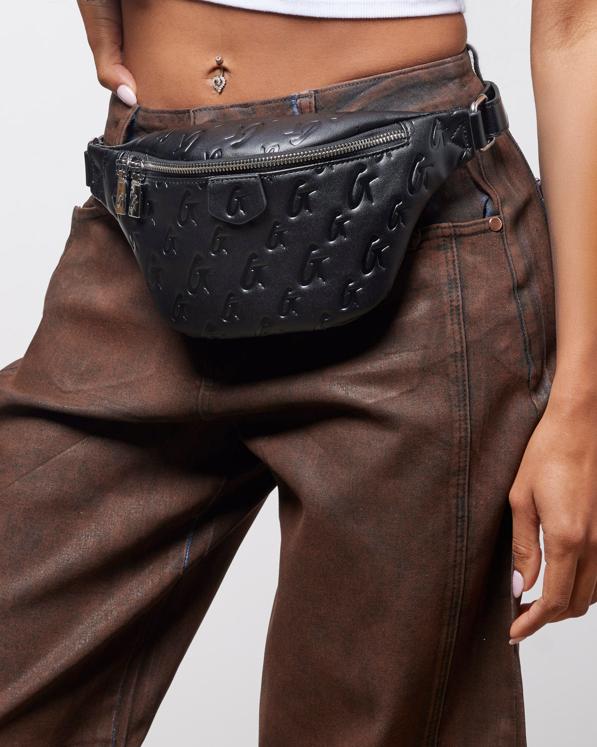 Black mini monogram fanny pack worn at the waist, featuring a zippered closure and embossed logo design.