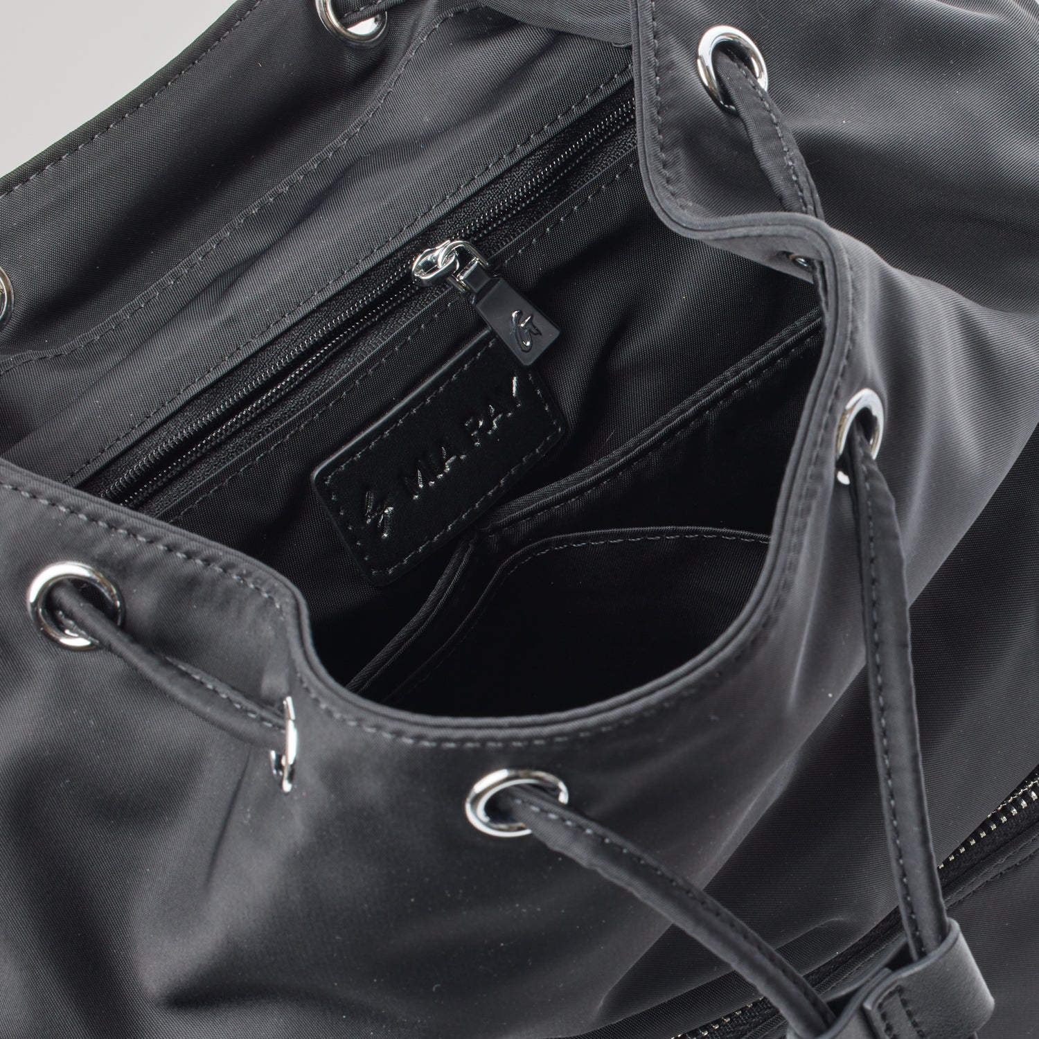 Black nylon backpack interior with multiple compartments, zippered pocket, and metal eyelet details.