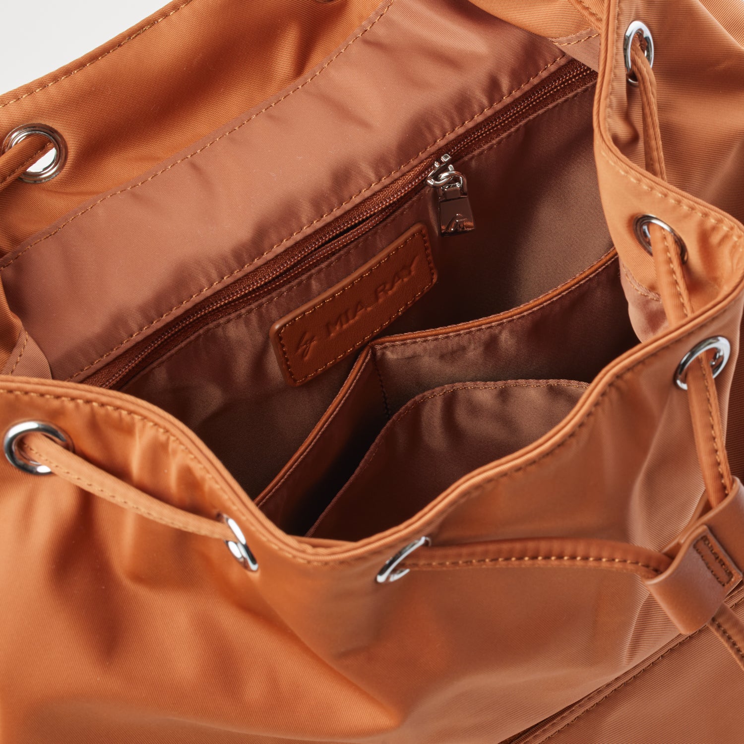 Inside view of a brown nylon backpack with multiple compartments, zippered pocket, and leather brand label.