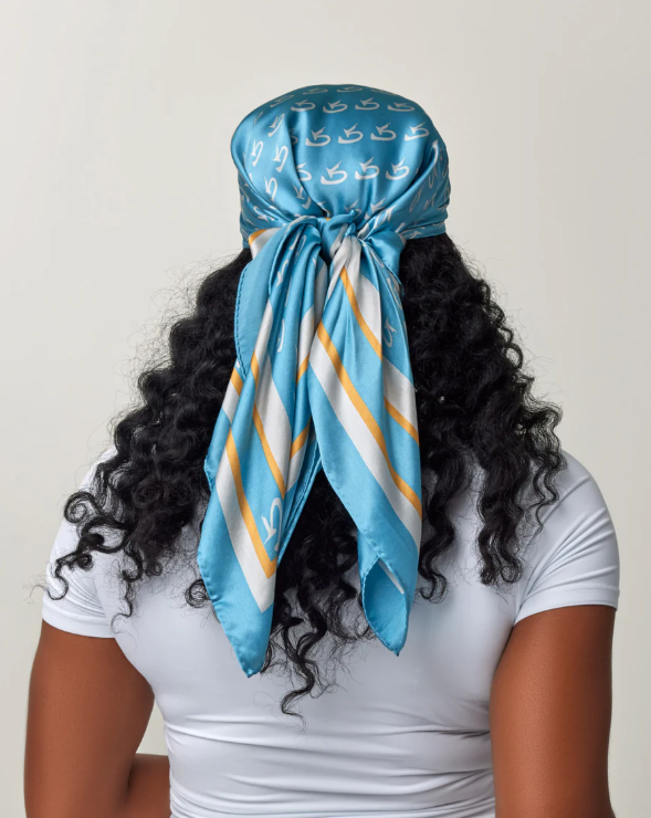 Silk scarf with blue, white, and gold stripes, featuring a white logo pattern, styled as a headwrap on a woman with curly ...