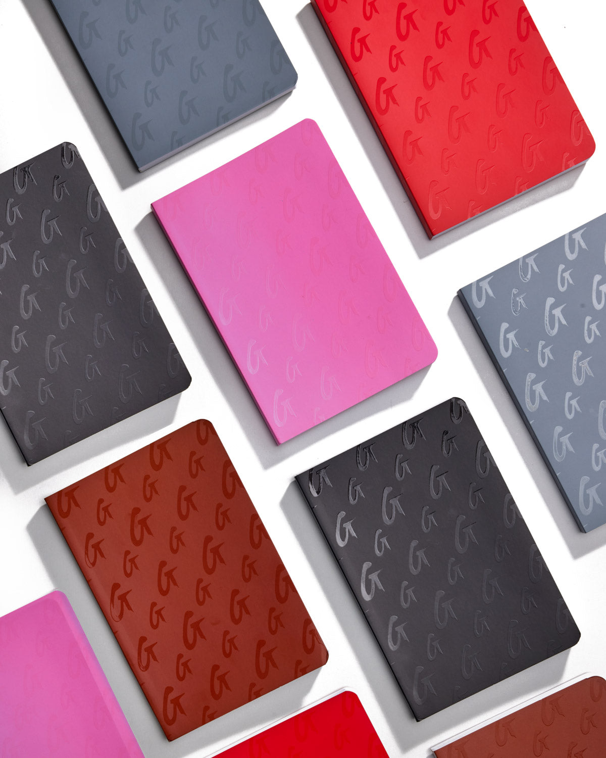 A collection of colorful Monogram Notebooks in black, red, pink, and gray with embossed monogram patterns on the covers.