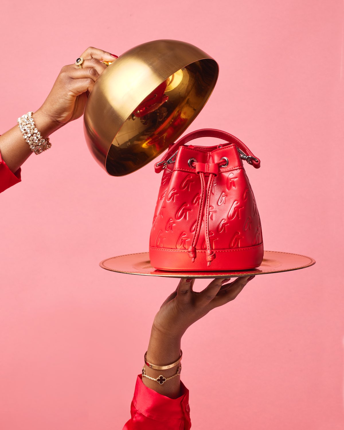 Red mini Monogram bucket bag with embossed logo pattern, drawstring closure, and top handle, displayed on a gold tray against a pink background.