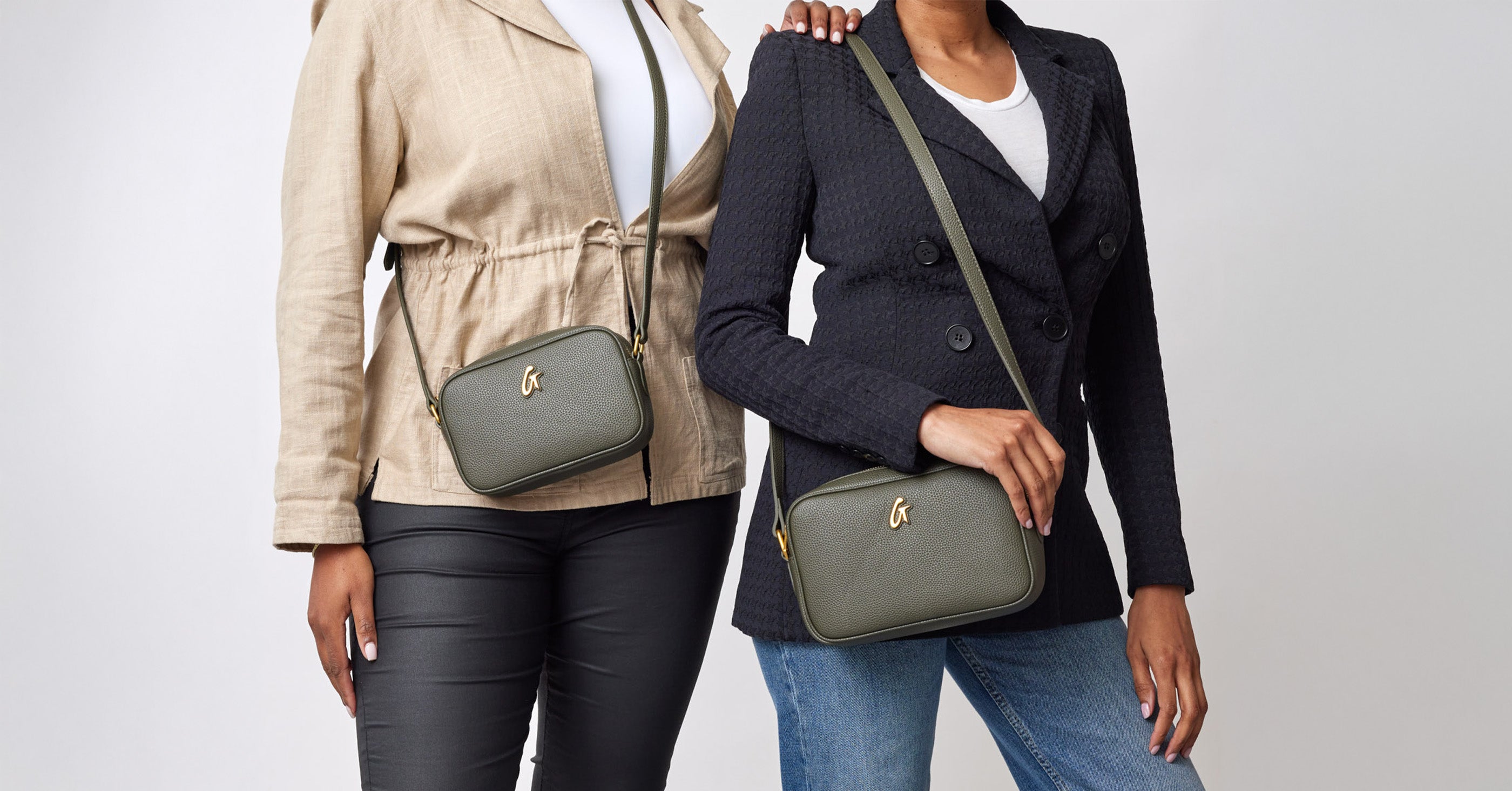 Two women hold matching olive green designer-style handbags with gold logo, pairing casual and blazer outfits.