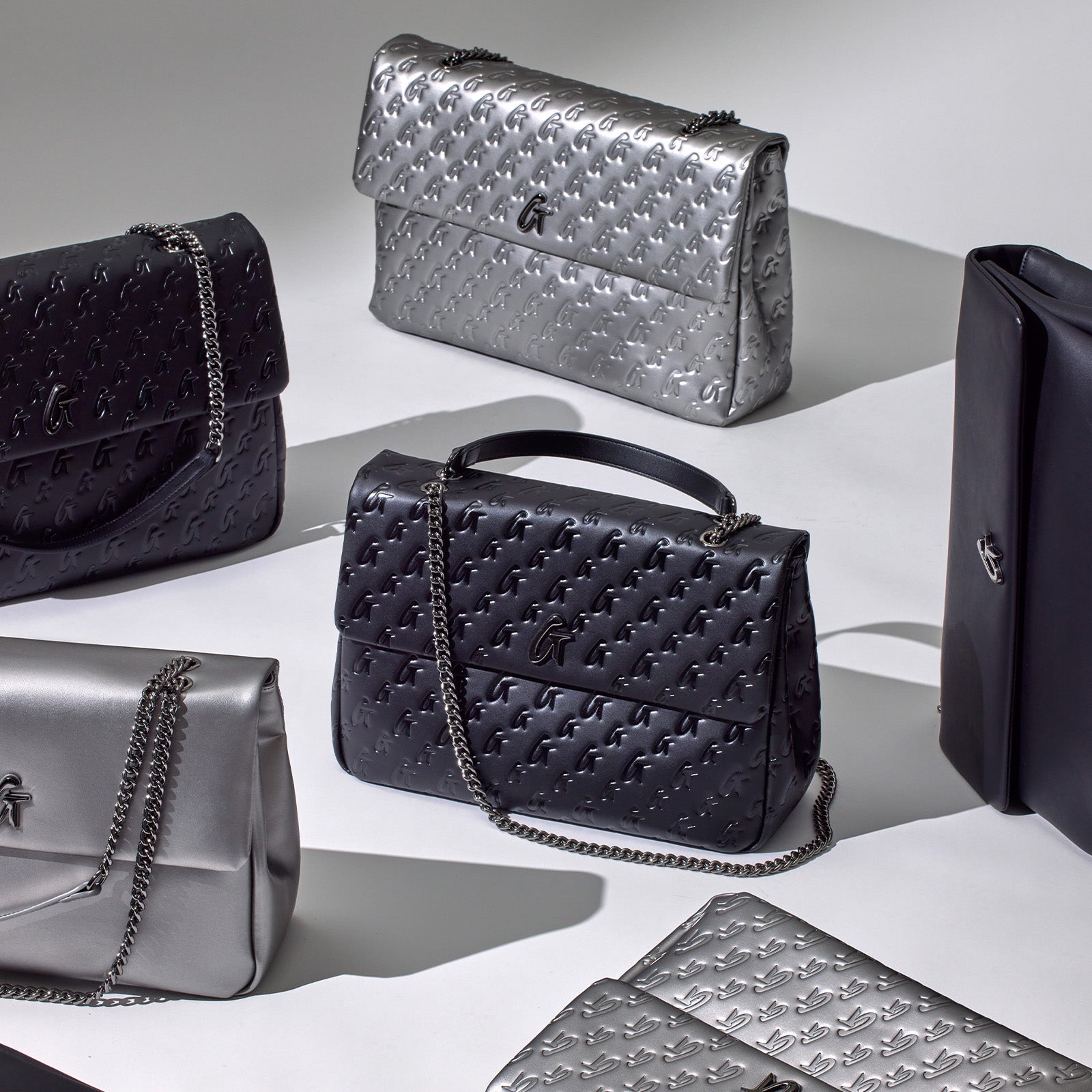 Assorted designer-style handbags in black, silver, and gray with embossed logo, chain straps, and sleek, affordable luxury...