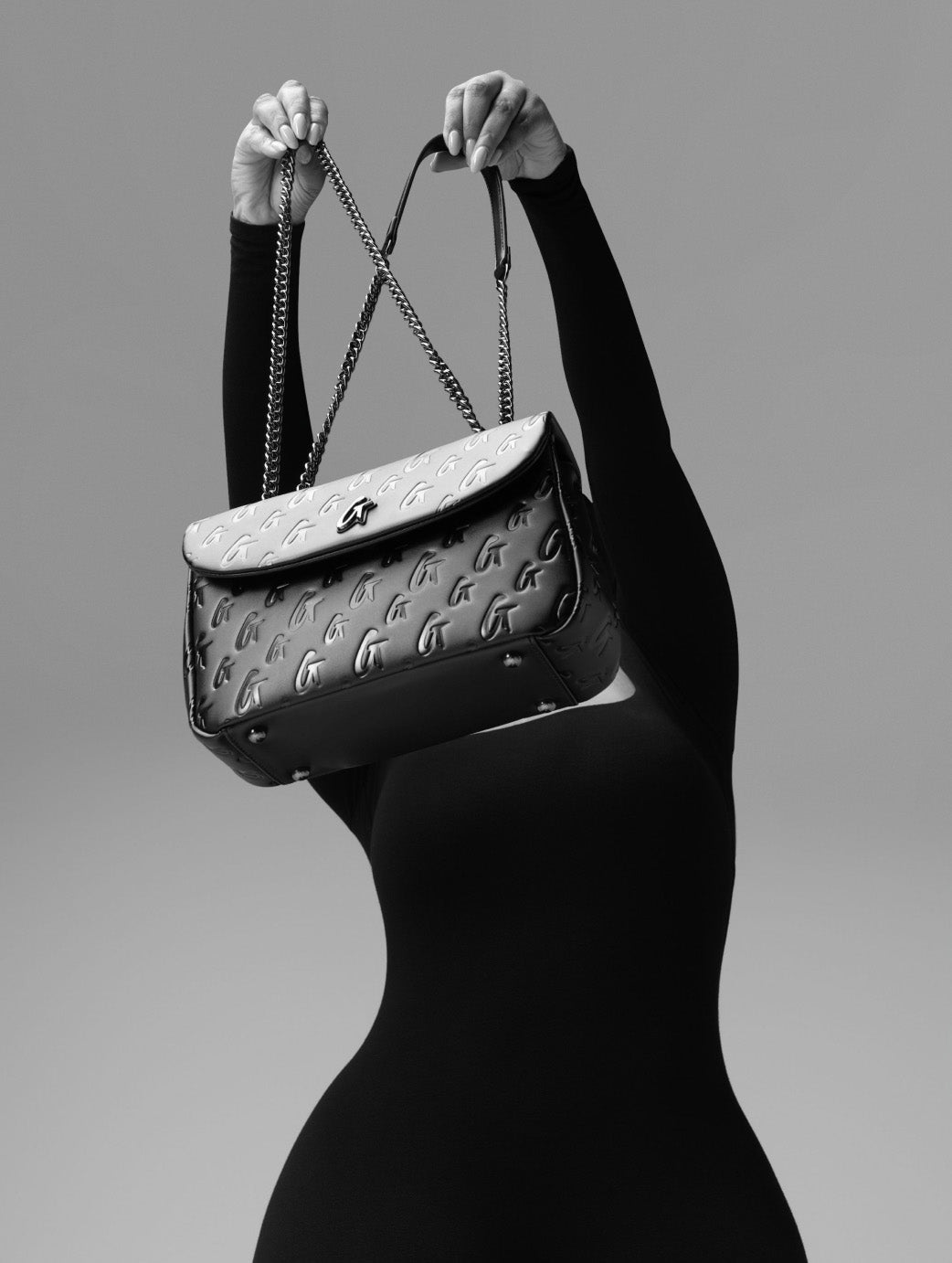 Black quilted handbag with silver chain strap, embossed logo pattern, and a sleek designer style for affordable luxury.