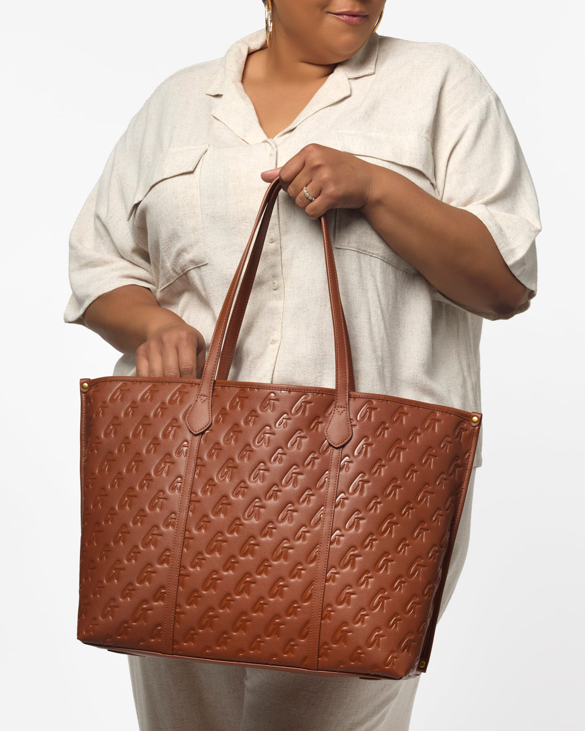 Brown XL monogram sleek tote held by a woman in a light-colored outfit, featuring embossed logo design and sturdy handles.