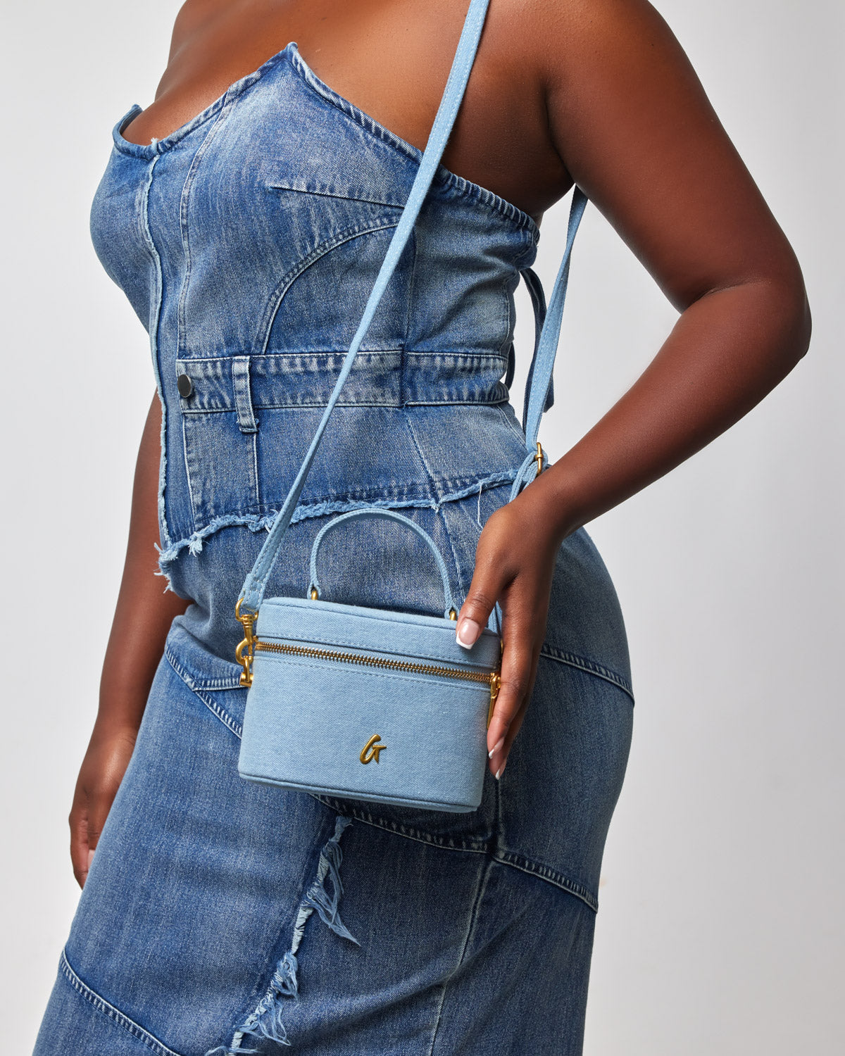 Mini denim gold vanity bag with a top handle, gold zipper, and a gold logo, worn crossbody with a denim outfit.