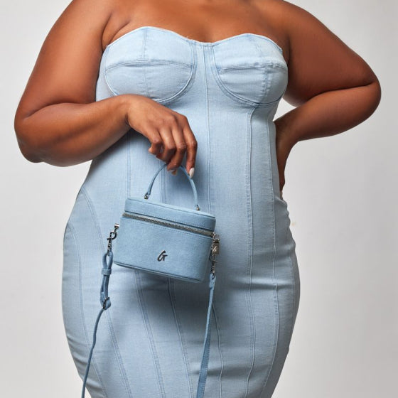 Plus-size woman in a light blue strapless dress holding a matching small handbag with a top handle and detachable shoulder...