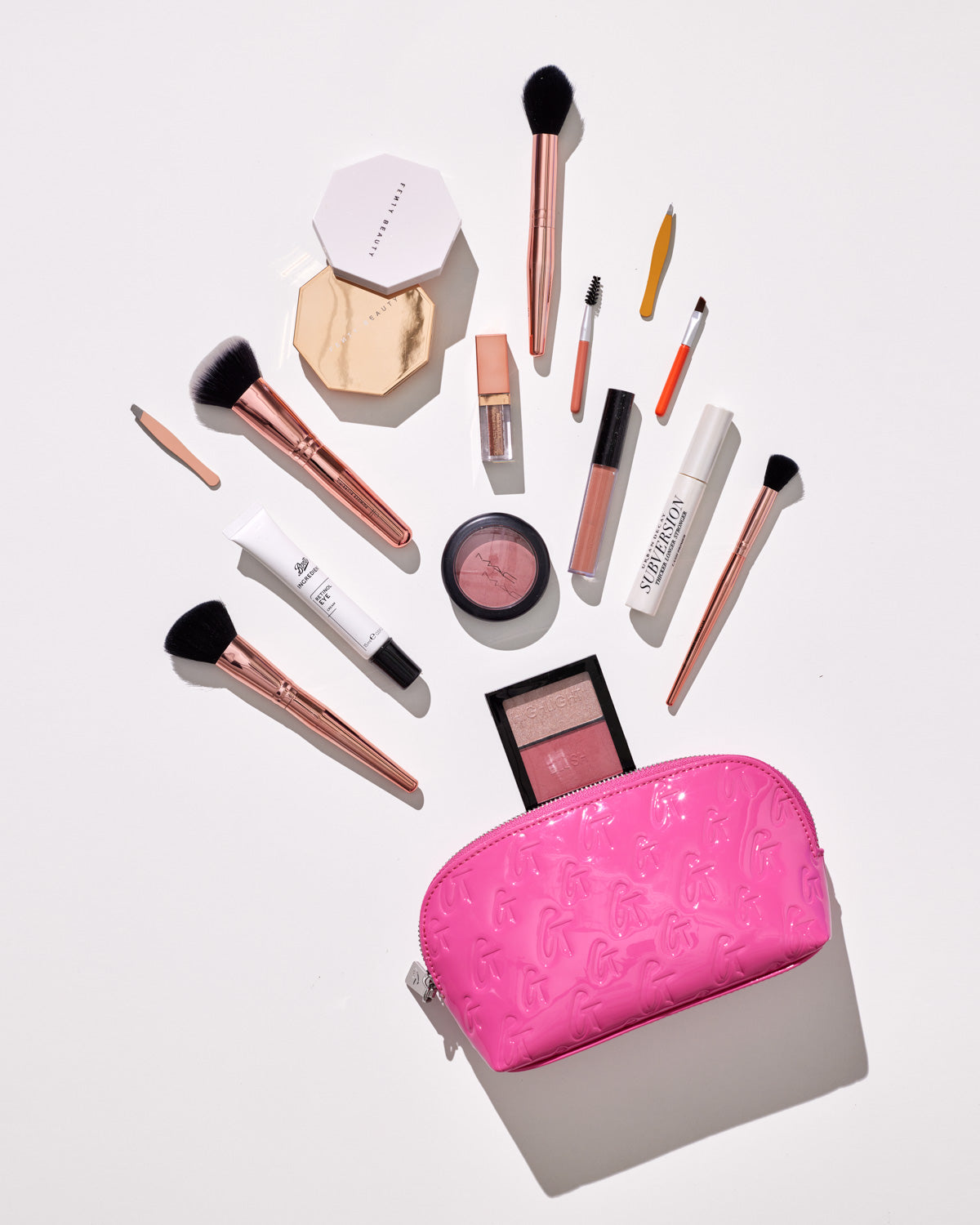 Pink monogram cosmetic pouch with embossed logo, open to reveal various makeup brushes, lip gloss, blush, and mirror.