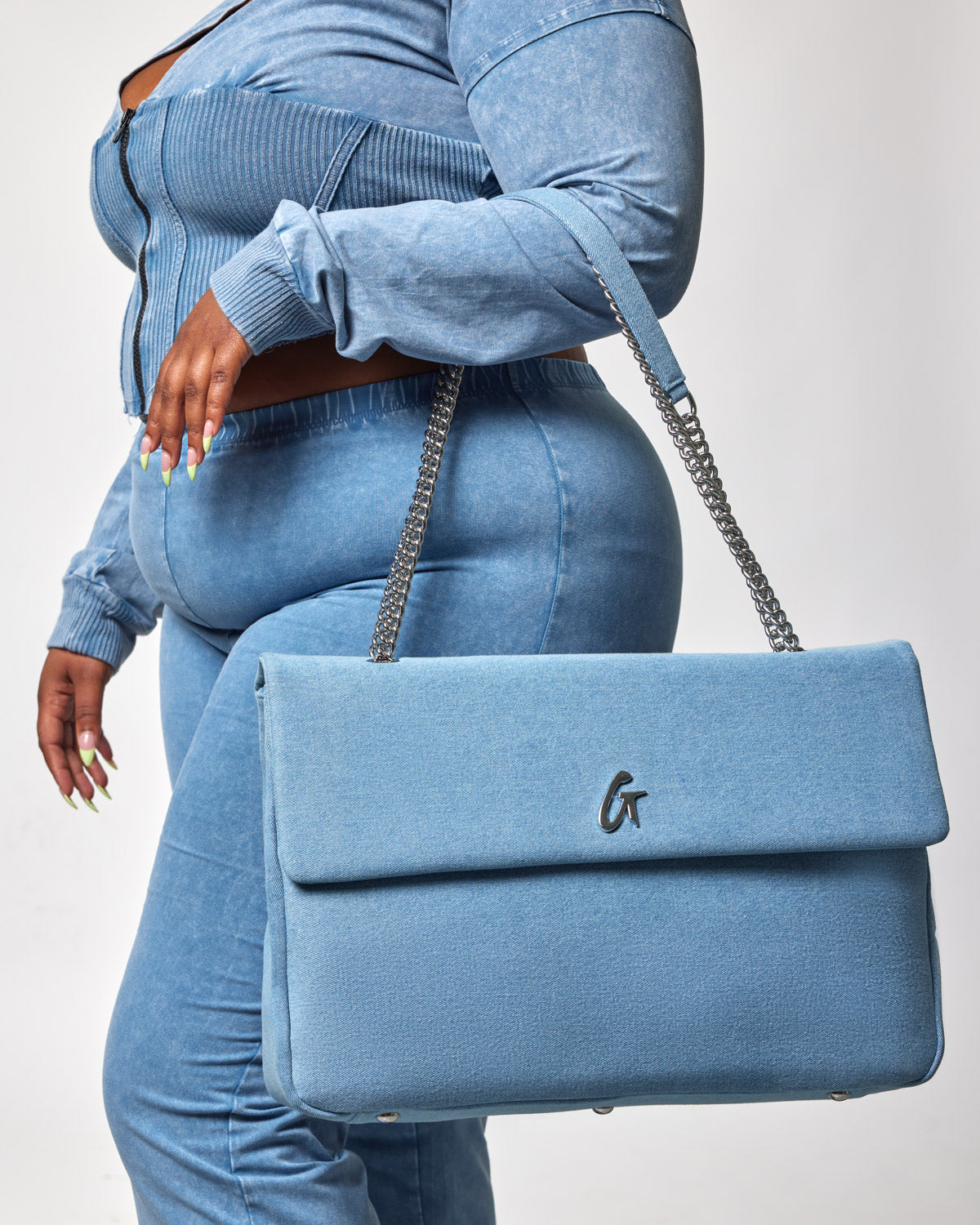 Blue denim XL flap bag with silver chain strap and a small logo on the front, carried by a person dressed in matching denim.