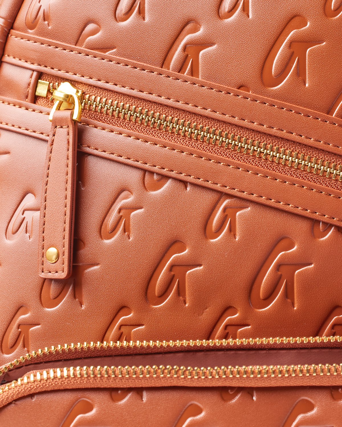 Close-up of a brown Monogram Unisex Backpack featuring embossed logo pattern and gold zipper details.