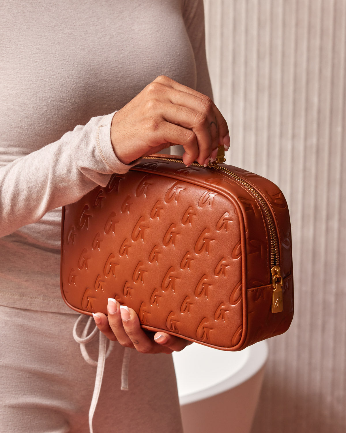 Small brown monogram toiletry bag with embossed G pattern, gold zipper, and compact rectangular shape.