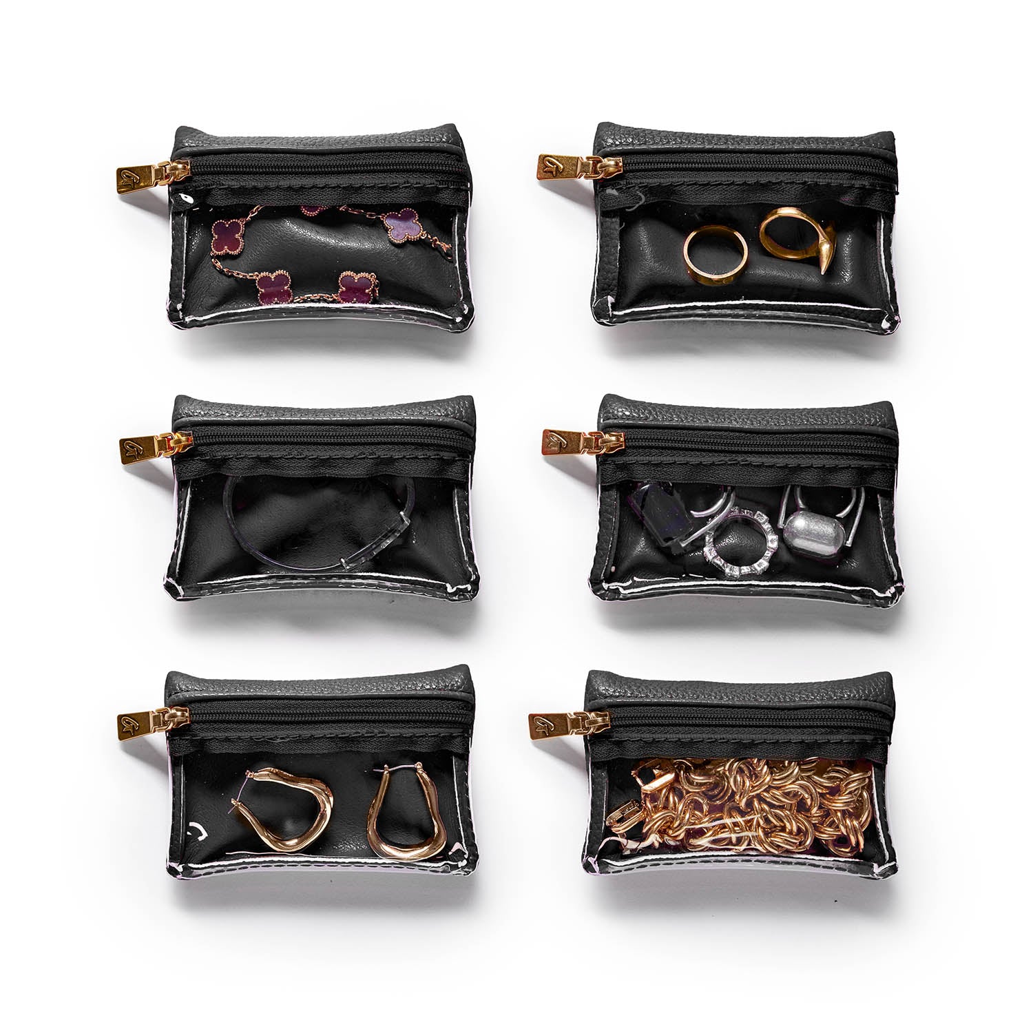 Six small black pebble jewelry cases with gold zippers, each containing different jewelry items like rings, earrings, and chains.