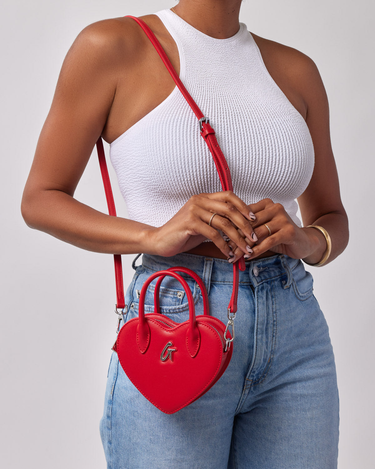 Red heart-shaped mini bag with a top handle and adjustable shoulder strap, worn across the body by a woman in a white tank top.
