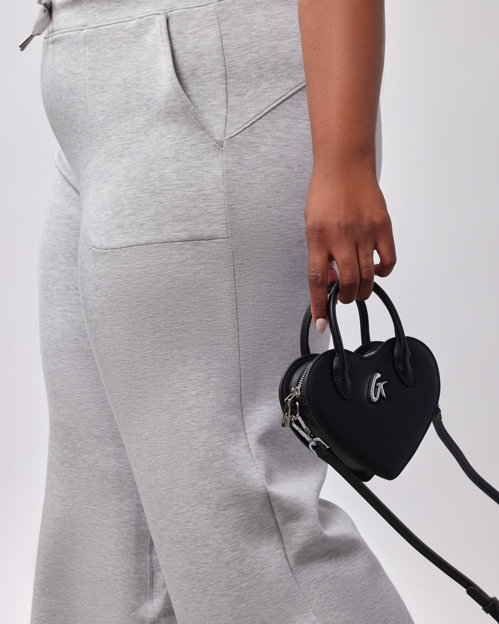 A person holding a small black heart-shaped bag with a top handle, silver hardware, and a detachable strap.