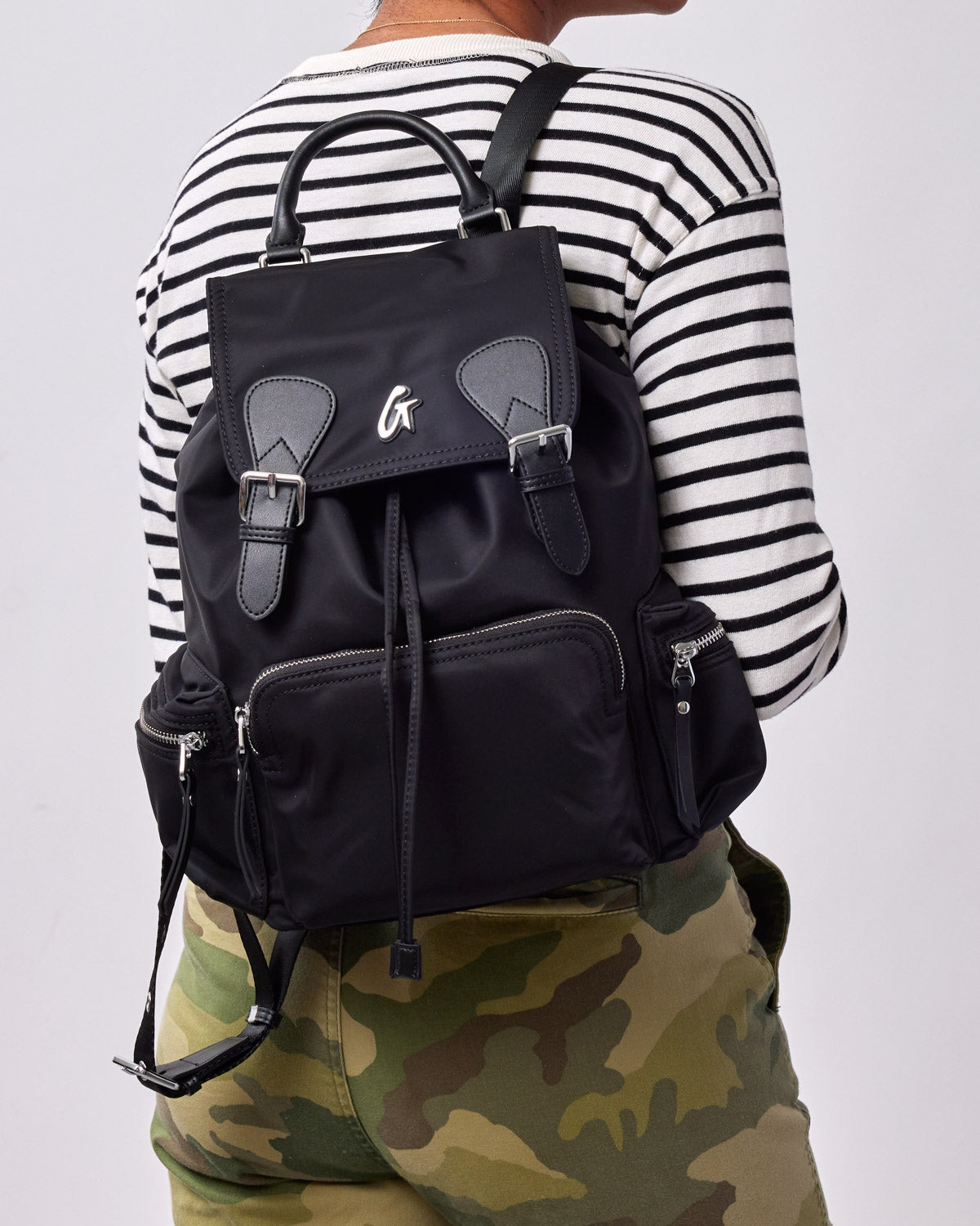 Black nylon backpack with multiple zippered compartments, adjustable straps, and a top handle, worn over a striped shirt.
