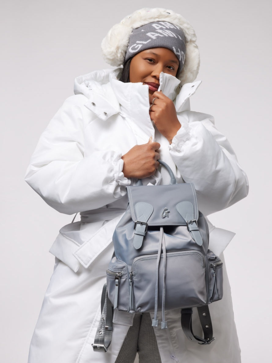 Gray nylon backpack styled with a cozy winter outfit, featuring a puffy white coat and a knit hat.