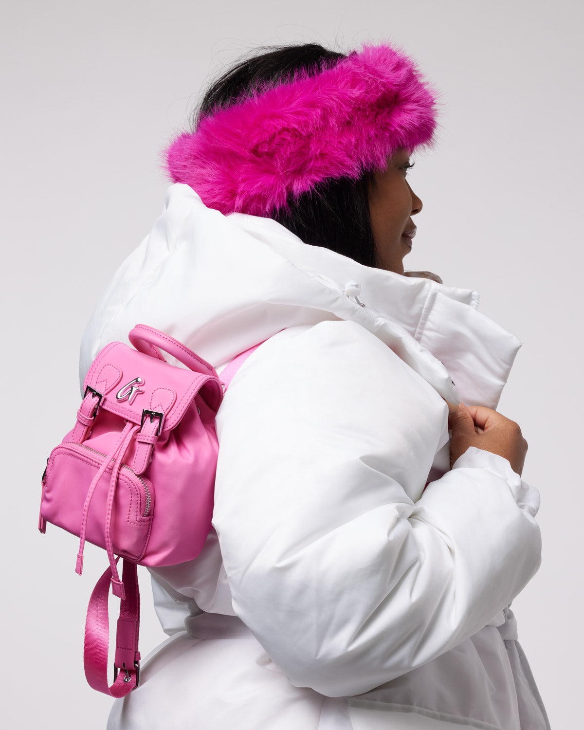 Hot pink mini nylon backpack worn on the back of a woman in a white puffer jacket, showcasing stylish functionality.