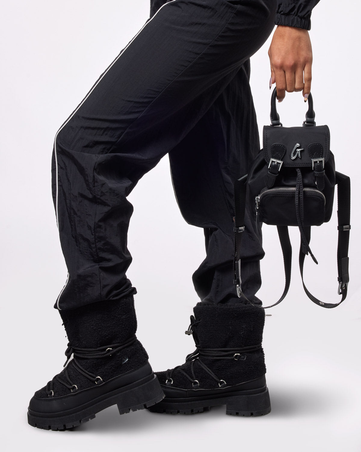 Stylish black mini nylon backpack held by a person in black pants and boots, perfect for a chic, casual look.