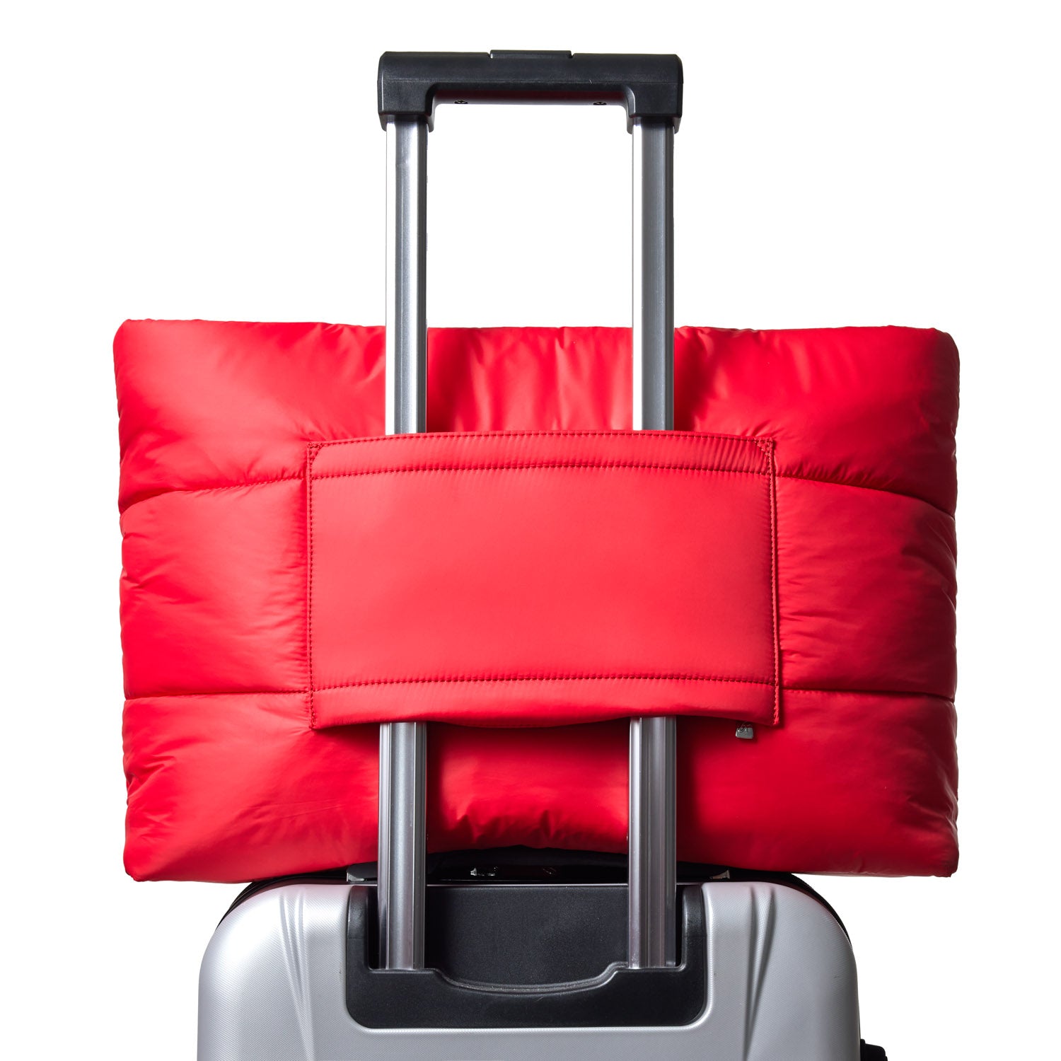Red athletic nylon tote bag secured on top of a silver suitcase, showcasing its practical design for travel.
