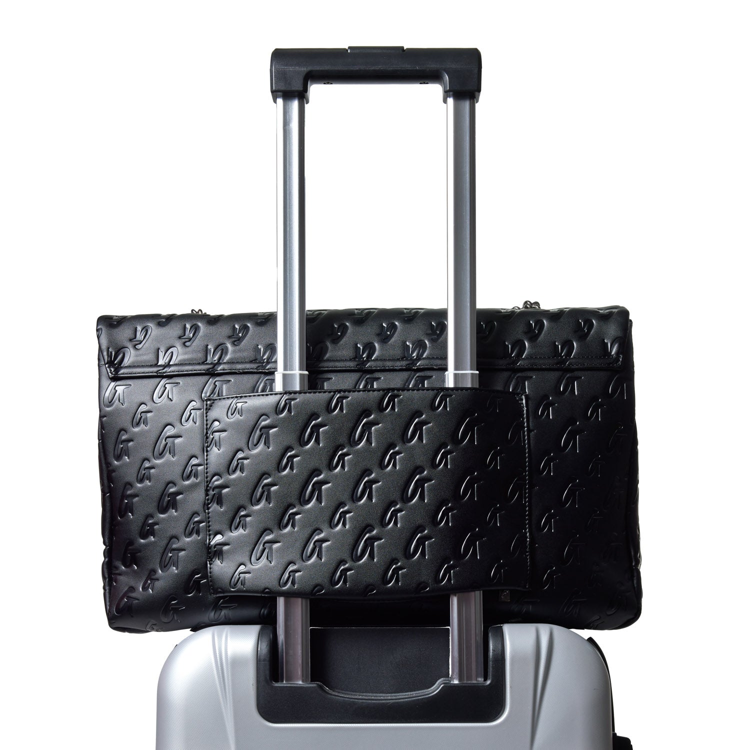 Large denim silver flap bag with embossed logo pattern, attached to a rolling suitcase handle for travel.