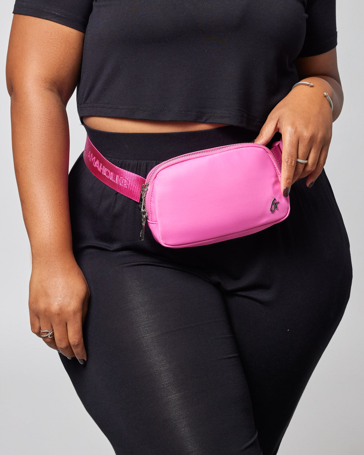 Pink nylon fanny pack worn around waist, featuring a zip closure and adjustable strap, styled with black clothing.