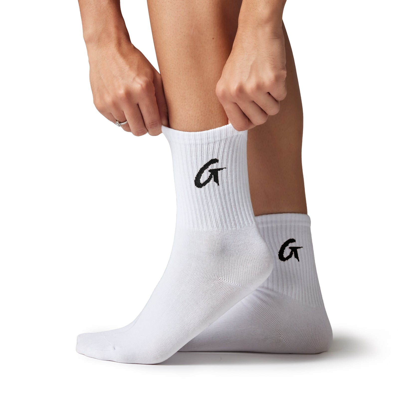 Pair of white crew socks with black "G" logo, worn by a person kneeling and adjusting the sock on one foot.