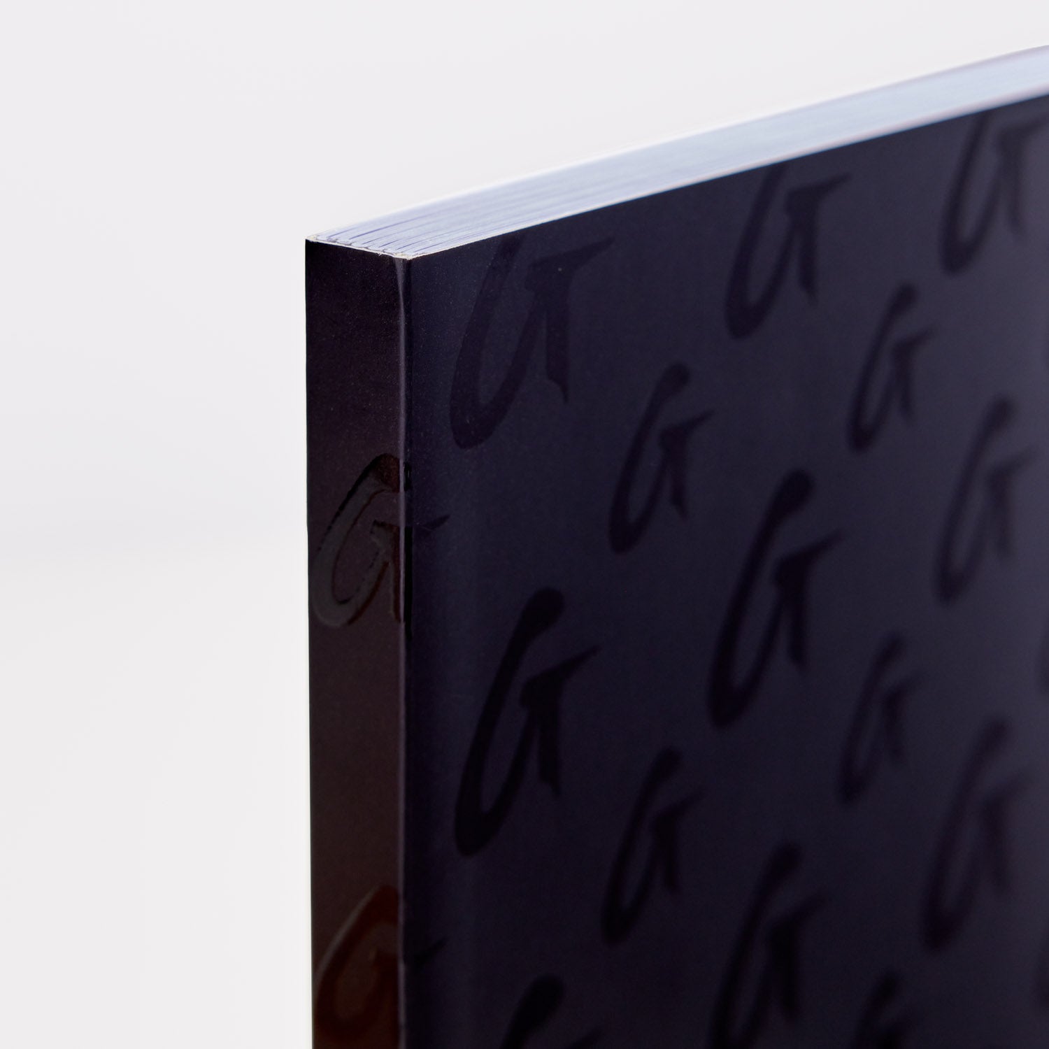 Close-up of a black monogram notebook with embossed pattern, showing the textured cover and white pages inside.