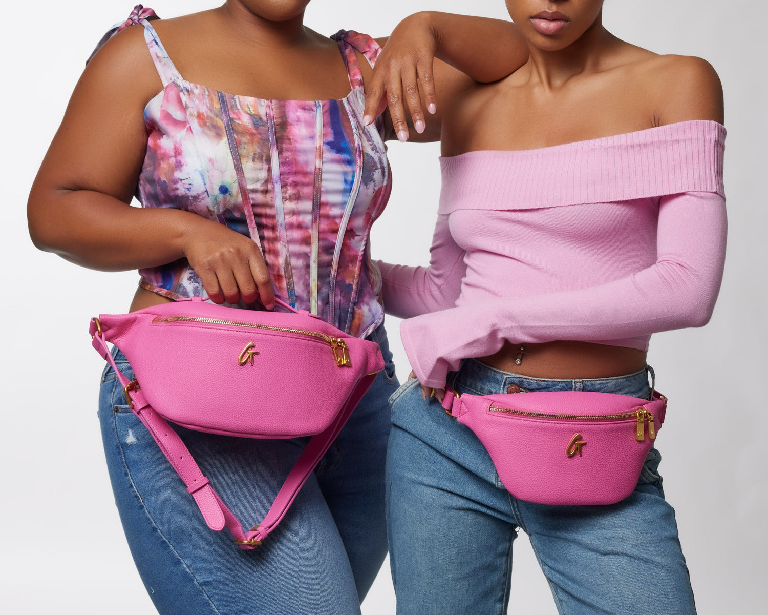 Two women wear pink mini pebble fanny packs around their waists, showcasing the stylish accessories in a fashion photo.