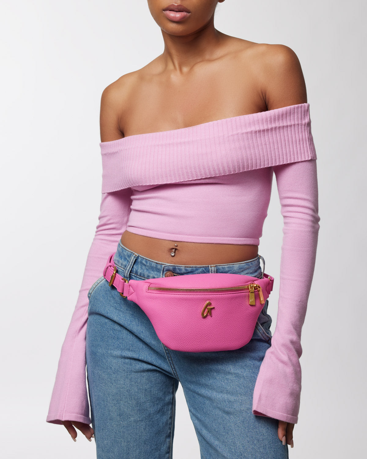 Pink Pebble Fanny Pack bundle worn around waist, featuring gold zipper and logo, styled with a pink off-shoulder top and jeans.