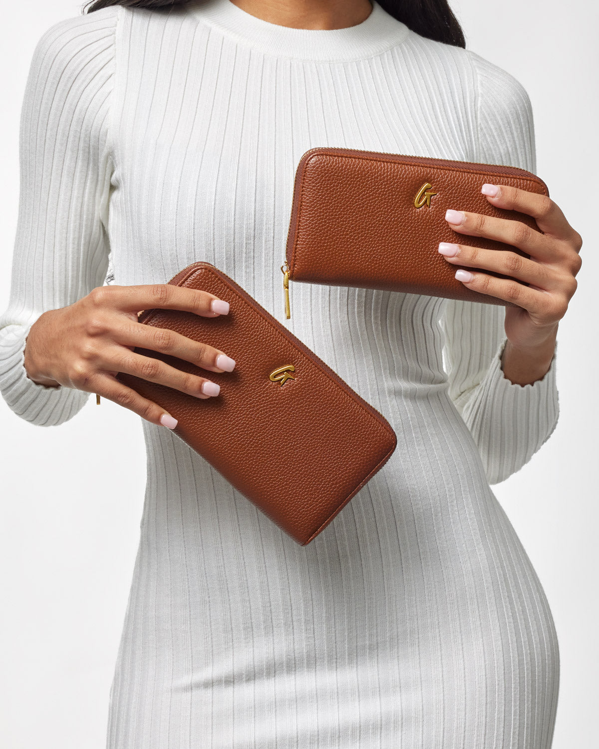 Brown textured pebble leather wallets with gold logo, held by a woman in a white ribbed dress.