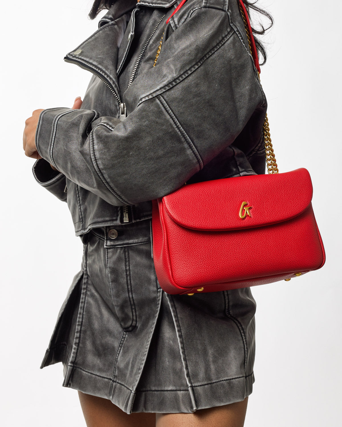 Red medium pebble flap bag with gold chain strap worn over a black denim jacket and skirt.