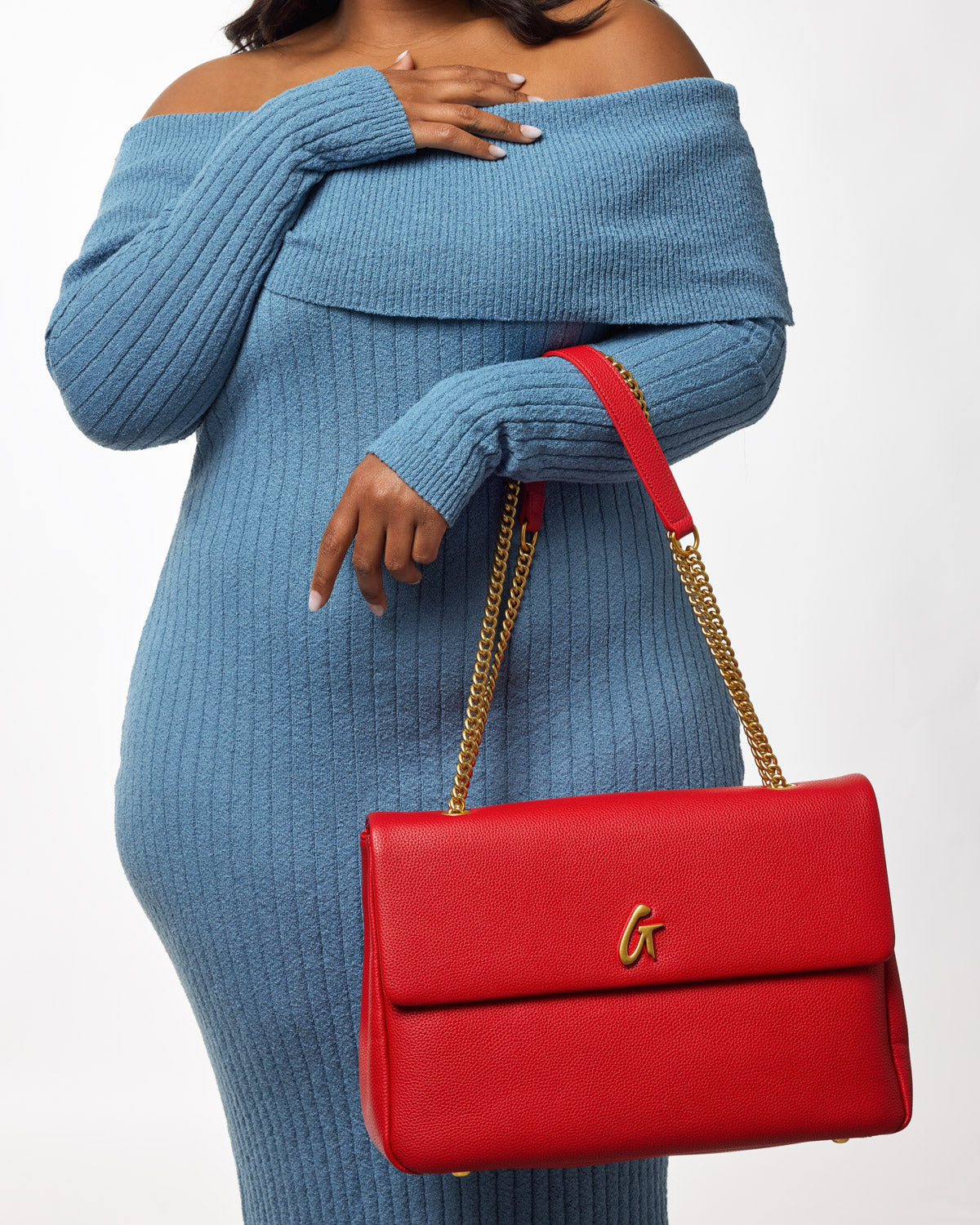 Large red pebble flap bag with gold chain strap, worn by a woman in a blue knit outfit.
