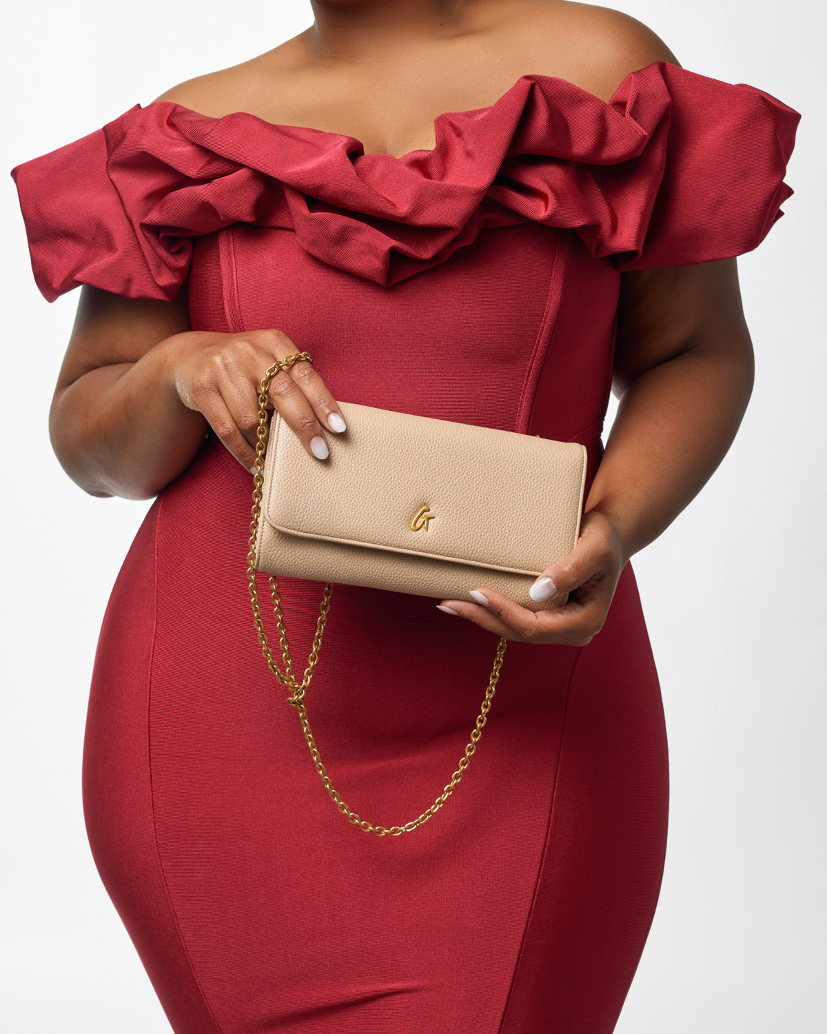 Beige Pebble Travel Wallet with gold chain, held by a woman in a red dress with ruffled neckline.