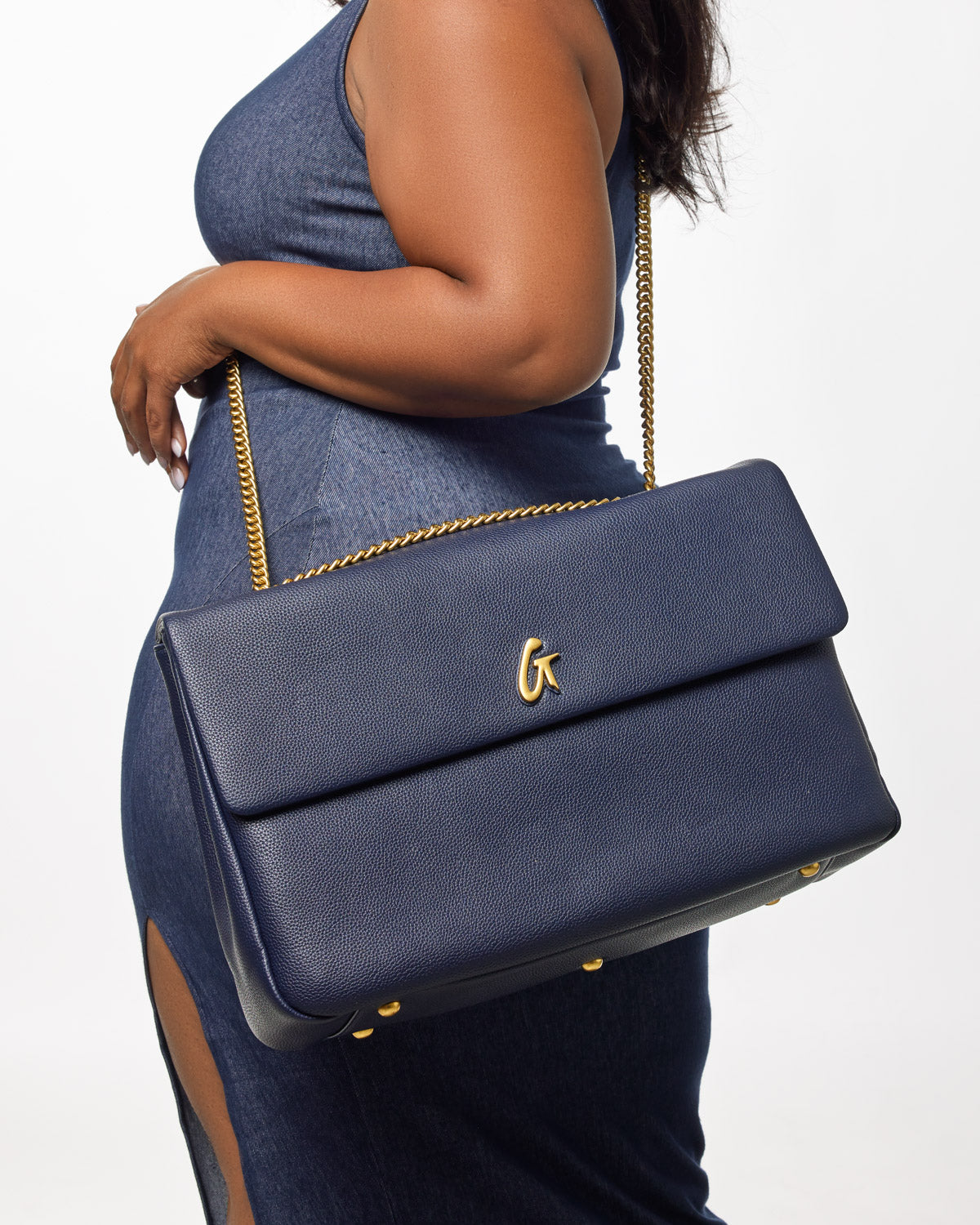 Large navy pebble leather flap bag with gold chain strap and gold "G" logo, worn over a denim outfit.