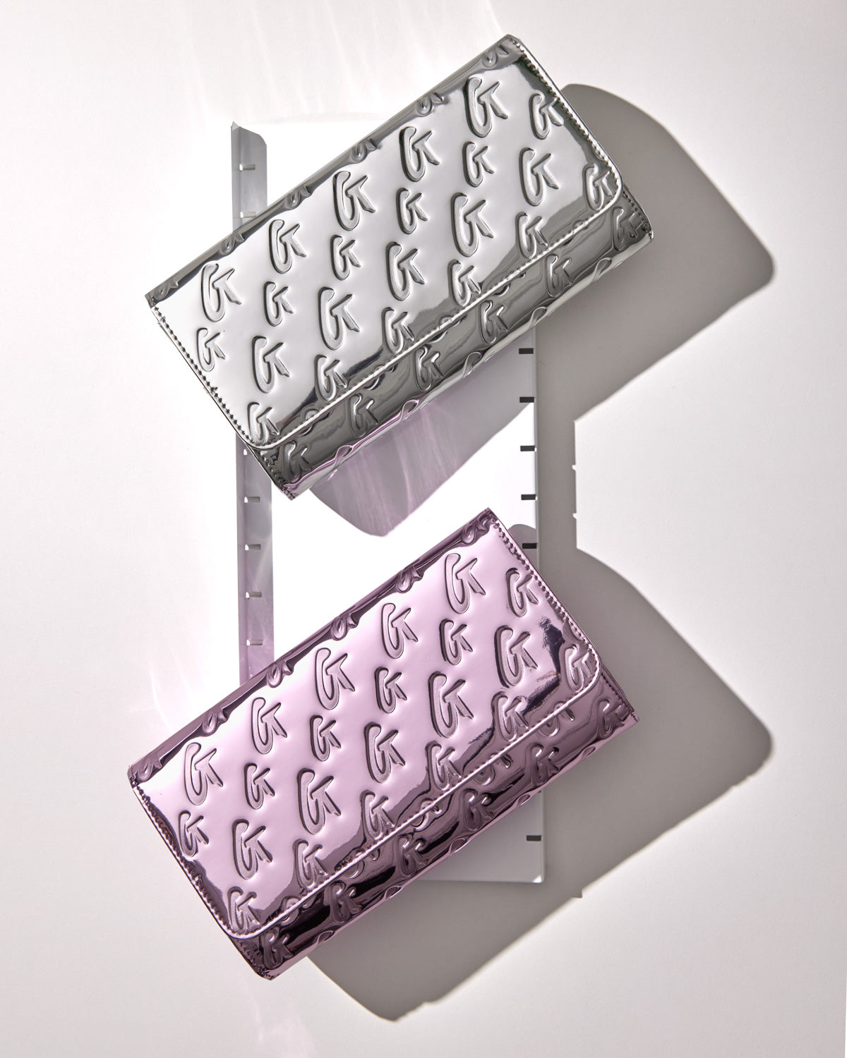 Metallic pink travel wallet with a monogram design, embossed with a repeating logo pattern, and a shiny, reflective finish.