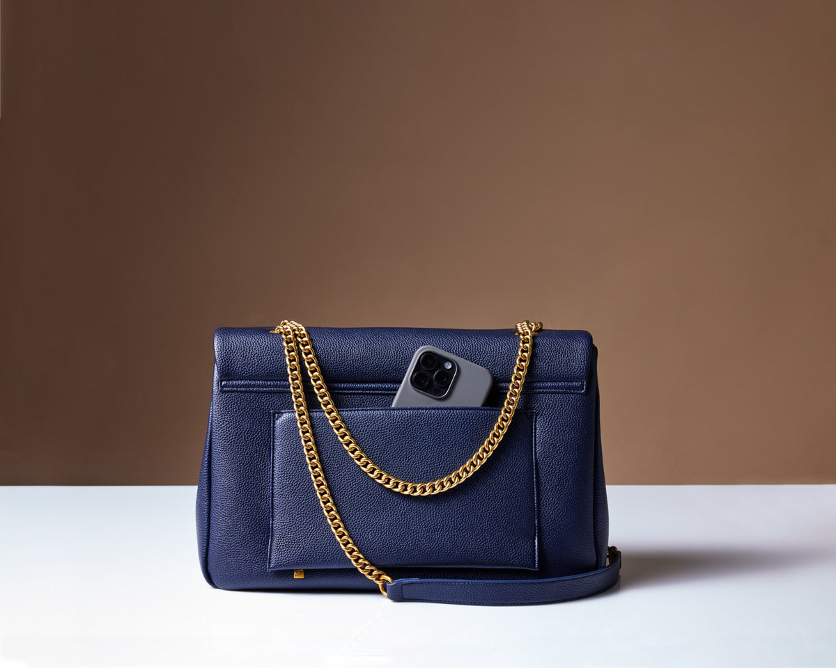Large navy pebble flap bag with a gold chain strap, featuring a front pocket and a smartphone partially visible inside.