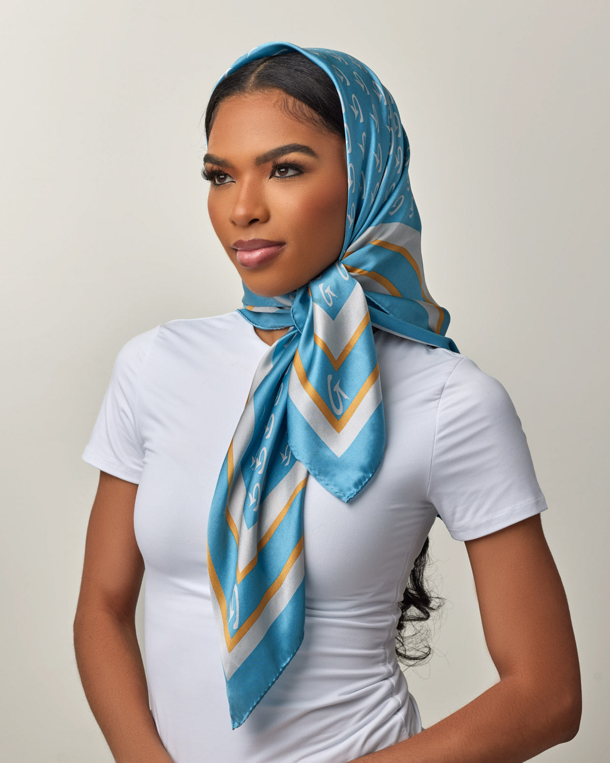 Model wearing a large blue and silver monogram silk scarf styled elegantly around her head and neck.