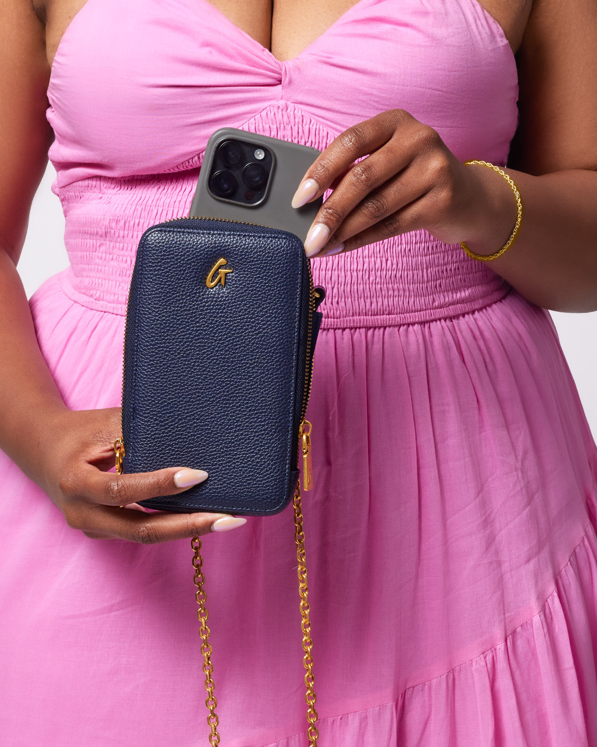 Navy Pebble Phone Crossbody bag with gold chain strap, holding a smartphone and a gray phone case.