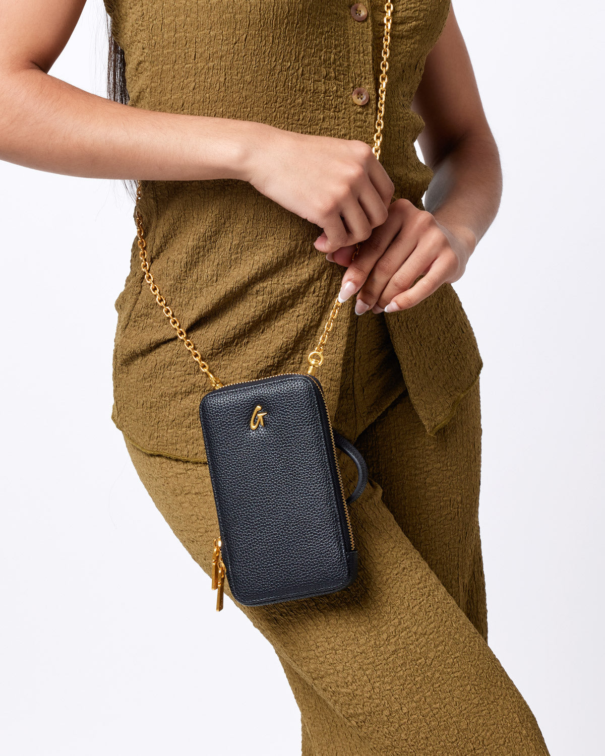Black Pebble Phone Crossbody bag with a gold chain strap and zipper, featuring a small gold logo on textured leather.