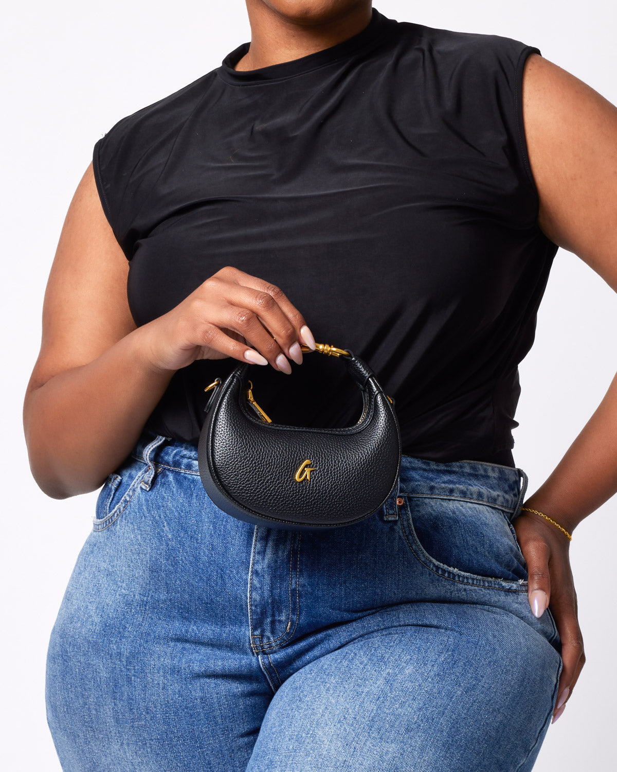 Black Nano Pebble Hobo Bag with gold accents, held by a woman wearing a black top and blue jeans.