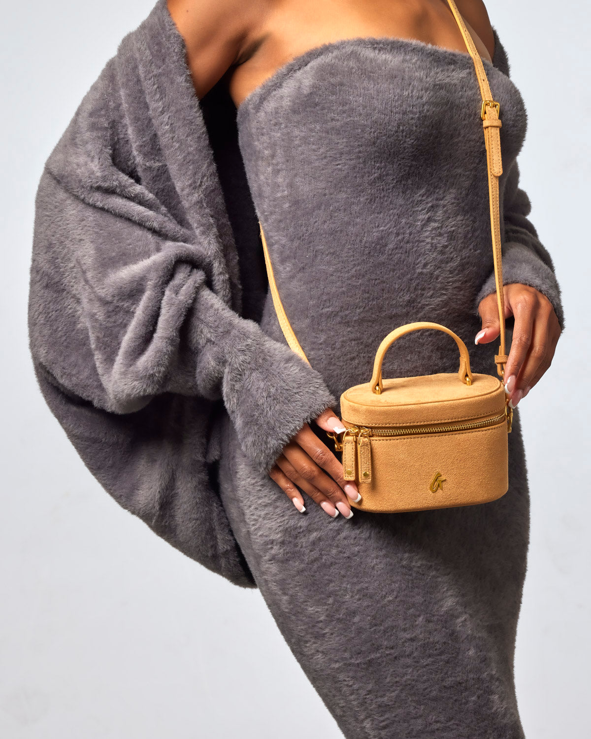 Tan mini suede vanity bag with a top handle and crossbody strap, styled with a cozy gray outfit.