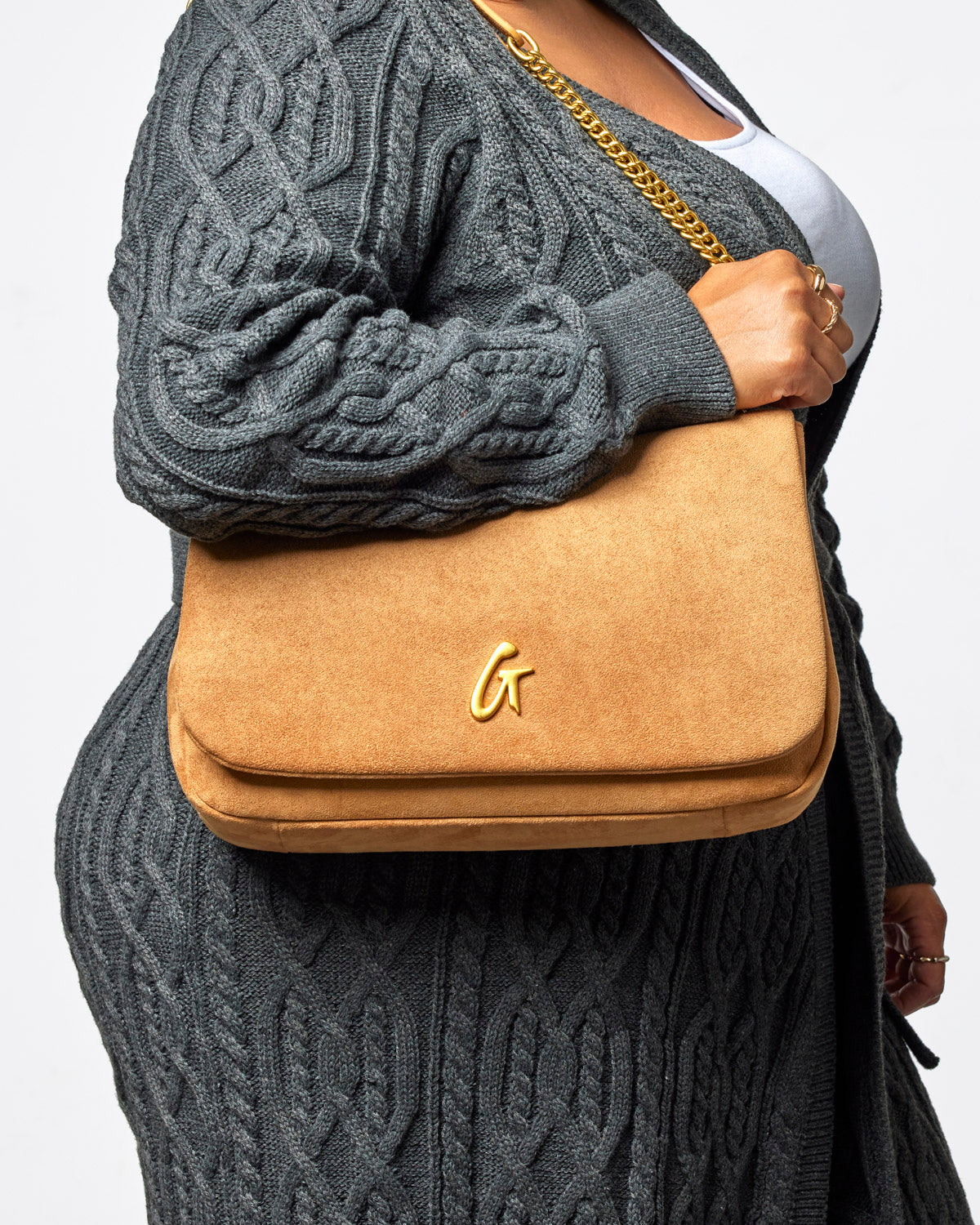 Medium tan suede flap bag with a gold chain strap, elegantly held by a woman in a cozy gray cardigan.
