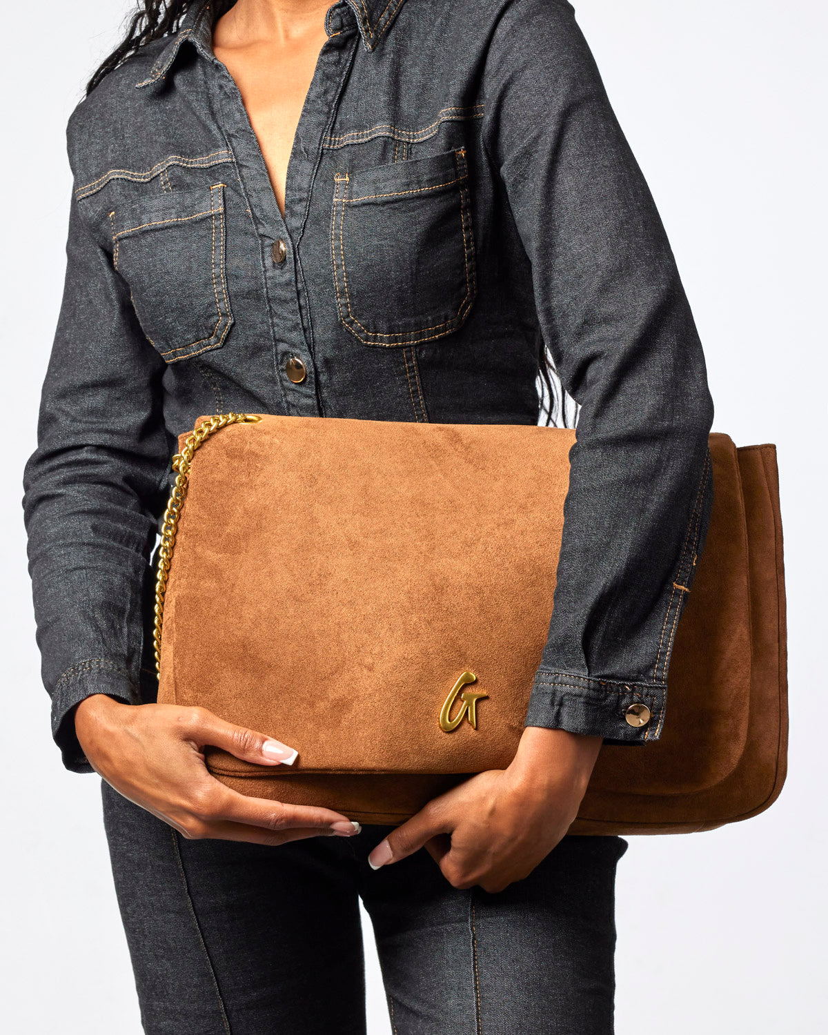 Large brown suede flap bag with a gold chain strap, held by a woman in a denim outfit. Stylish and versatile accessory.