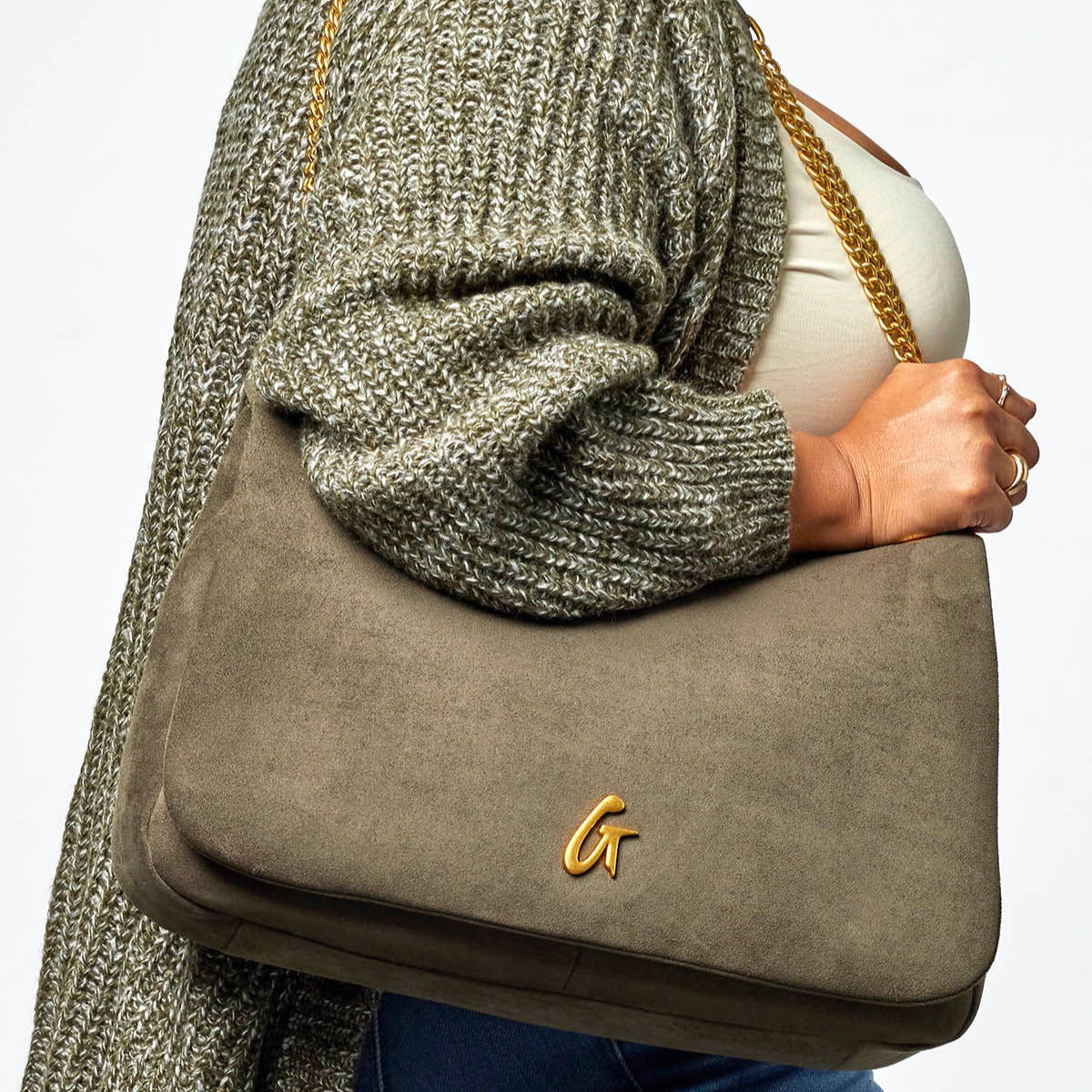 Olive green large suede flap bag with gold chain strap, styled with a cozy sweater for a chic look.