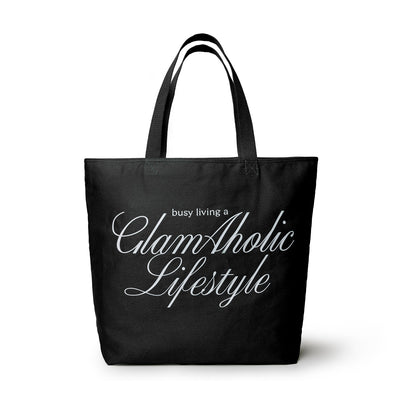 Black canvas tote bag featuring the phrase "busy living a GlamAholic Lifestyle" in elegant white lettering.