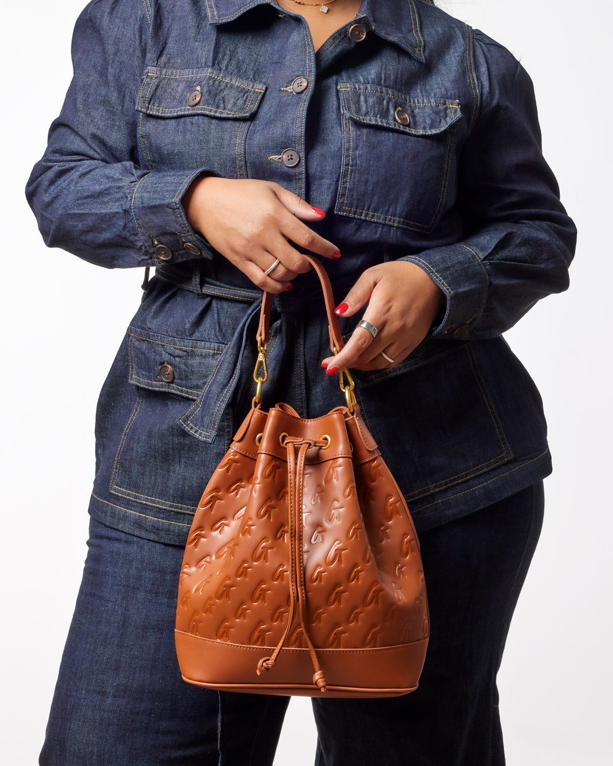 Large brown monogram bucket bag held by a woman in a denim jacket, showcasing its stylish design and versatility.