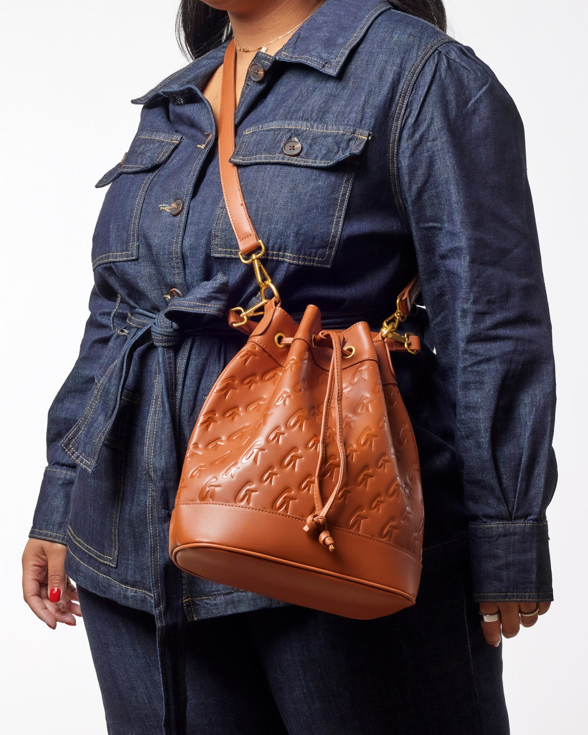 Large brown monogram bucket bag with drawstring closure, worn crossbody by a model in a denim jacket.