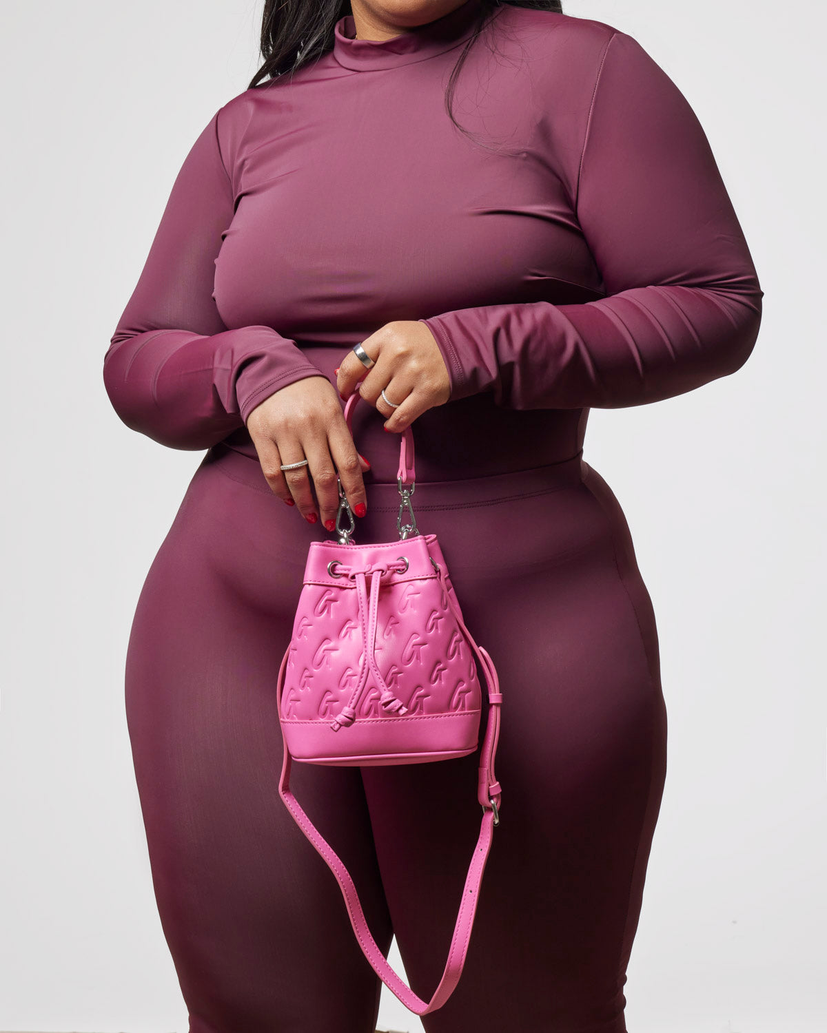 Hot pink mini monogram bucket bag held by a model in a fitted burgundy outfit, showcasing stylish luxury.
