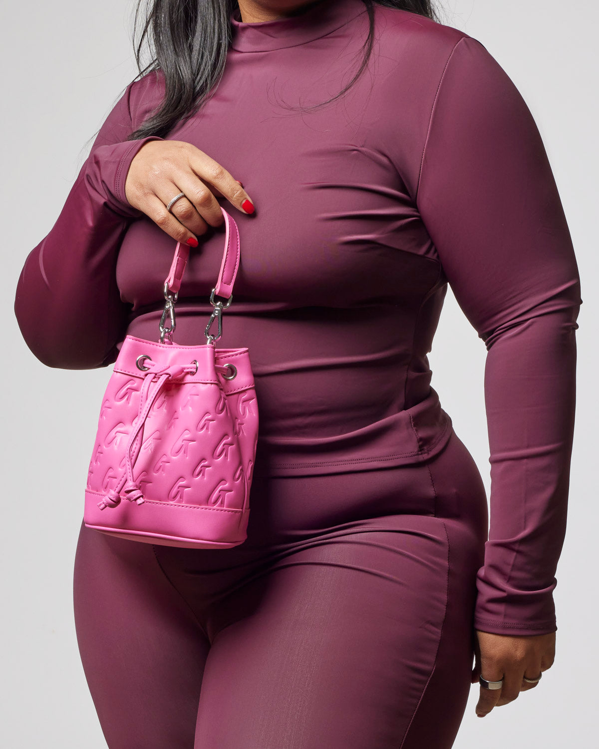 Hot pink mini monogram bucket bag held by a woman in a fitted burgundy outfit, showcasing affordable luxury style.